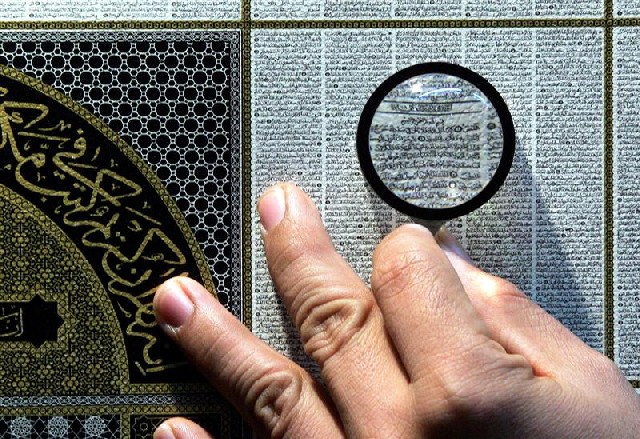 An Indonesian Muslim uses magnifying glass to read Koran verses printed on lamb parchment, Jakarta, July 27, 2005/Beawiharta